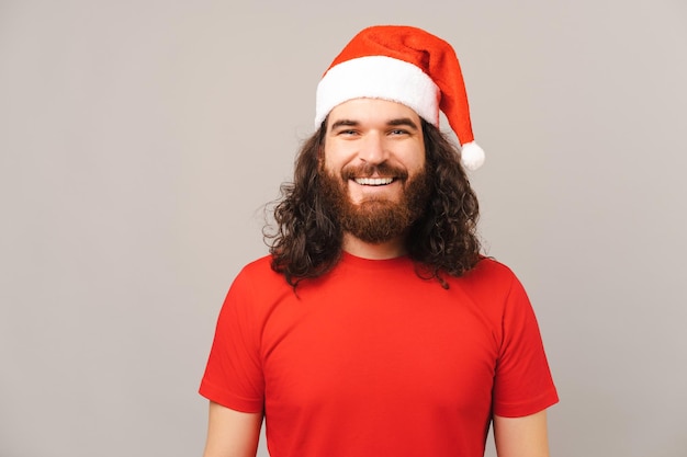 Un apuesto hombre barbudo con gorra roja de Navidad sonríe a la cámara