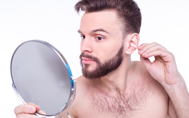 Un apuesto hombre barbudo se limpia la oreja con un bastoncillo de algodón o palitos para la oreja
