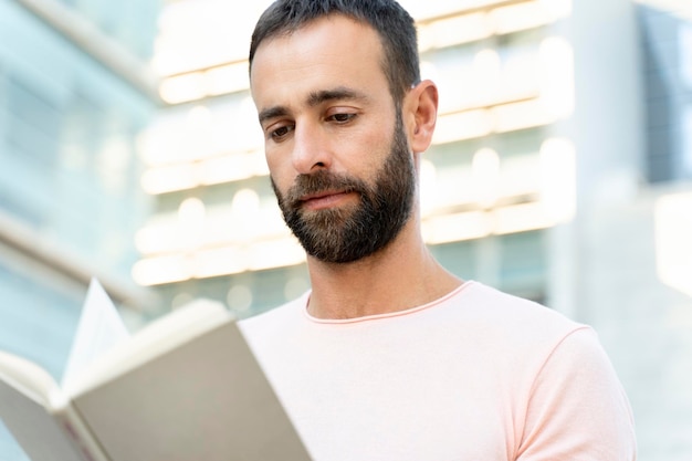 Foto apuesto hombre barbudo de mediana edad leyendo un libro, planificando un proyecto en la calle