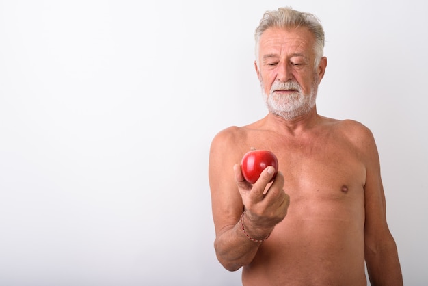 Apuesto hombre barbudo senior mirando manzana roja descamisados sobre blanco