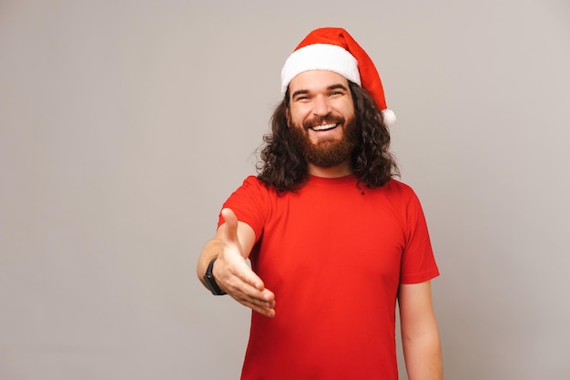 Un apuesto hombre barbudo con sombrero de Navidad ofrece su mano para saludarte