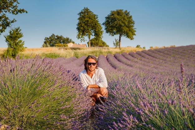 El apuesto hombre brutal con cabello largo y moreno se sienta en el campo de lavanda en provence cerca de valensole