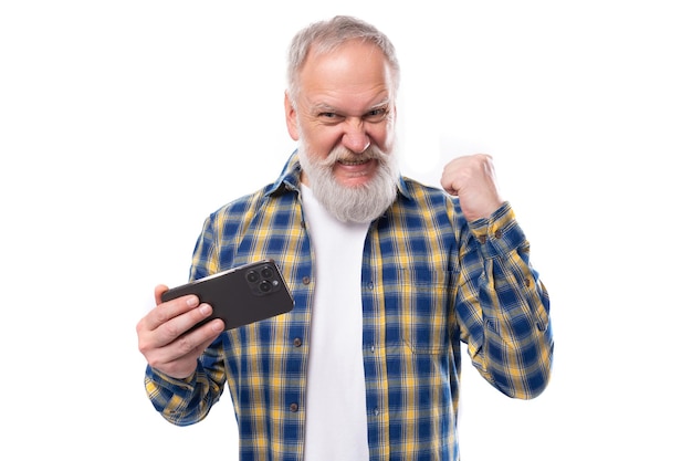 Apuesto hombre canoso de mediana edad con barba en una camisa se regocija sosteniendo un teléfono en un blanco