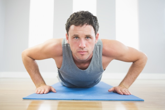 Foto apuesto hombre deportivo haciendo flexiones en la alfombra azul