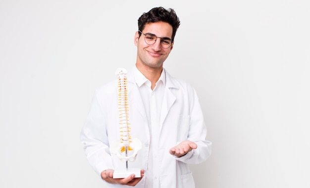 Apuesto hombre hispano sonriendo felizmente con amabilidad y ofreciendo y mostrando un concepto de especialista en columna vertebral