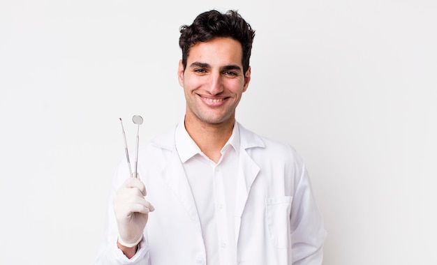 Apuesto hombre hispano sonriendo felizmente con una mano en la cadera y un concepto de dentista confiado