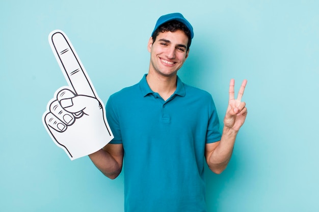 Apuesto hombre hispano sonriendo y luciendo amigable mostrando el concepto de ventilador de mano número dos número uno