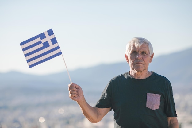 Apuesto hombre jubilado con cabello gris sosteniendo la bandera de Grecia símbolo nacional de Grecia