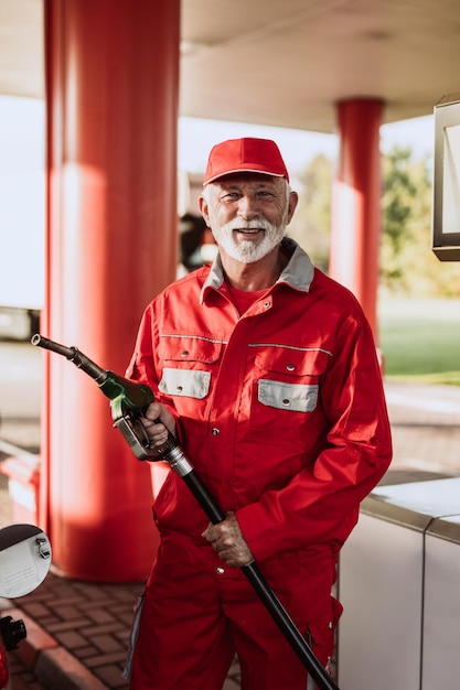 Un apuesto hombre mayor con barba trabajando en una gasolinera.