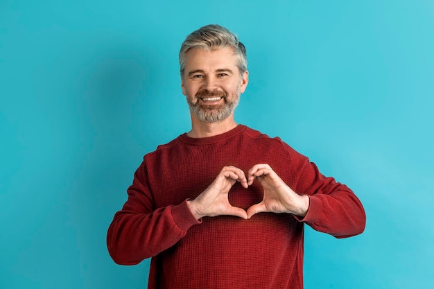 Apuesto hombre de mediana edad sosteniendo el símbolo del corazón en azul