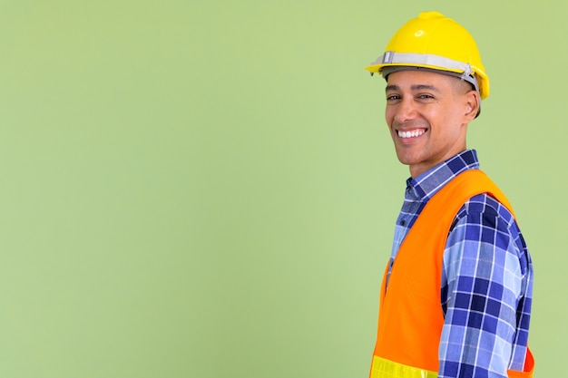 Apuesto hombre multiétnico trabajador de la construcción contra la pared de color