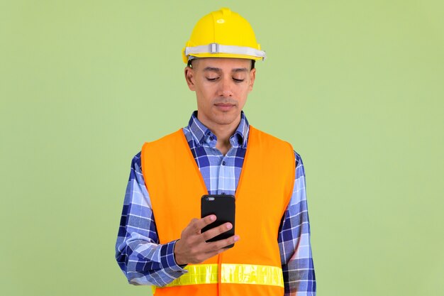 Apuesto hombre multiétnico trabajador de la construcción contra la pared de color