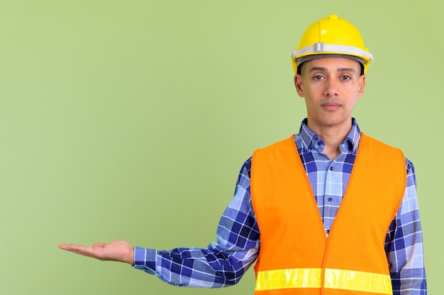 Apuesto hombre multiétnico trabajador de la construcción contra la pared de color