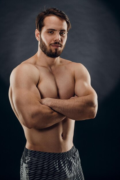 Un apuesto hombre musculoso sin camiseta posa para un fotógrafo en un estudio fotográfico oscuro El concepto de deporte