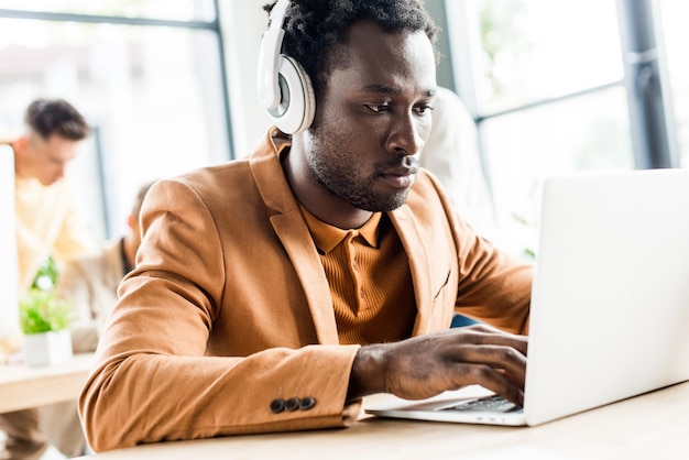 Apuesto hombre de negocios afroamericano en auriculares usando laptop