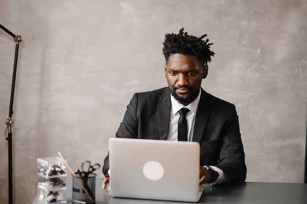 Apuesto hombre de negocios afroamericano en traje clásico usa laptop