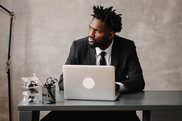 Apuesto hombre de negocios afroamericano en traje clásico usa laptop