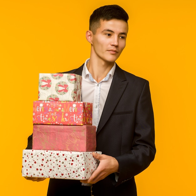 Apuesto hombre de negocios asiático con caja de regalo sobre fondo amarillo