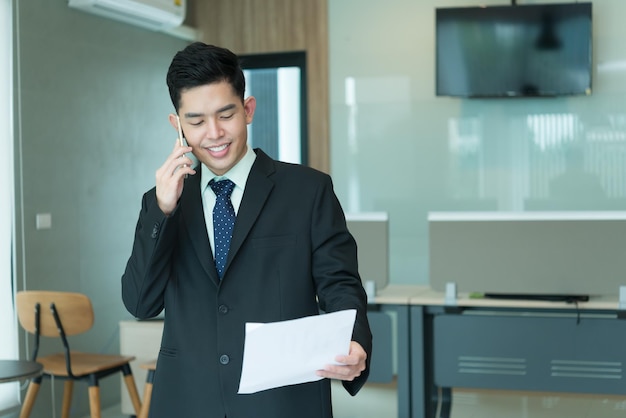 Un apuesto hombre de negocios asiático lee un archivo en la oficina. Un hombre de negocios tailandés habla por teléfono con su jefe.