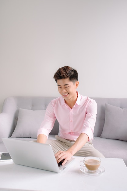 Apuesto hombre de negocios asiático sonriendo mientras trabaja con una computadora portátil en casa