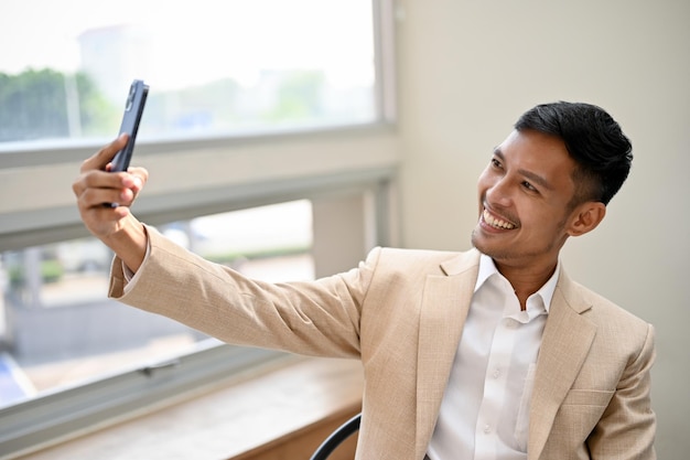 Apuesto hombre de negocios asiático tomando un selfie o grabando un video en su teléfono inteligente