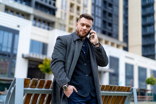 Un apuesto hombre de negocios confiado tiene una llamada telefónica. Hombre elegante caminando por las calles de la ciudad.