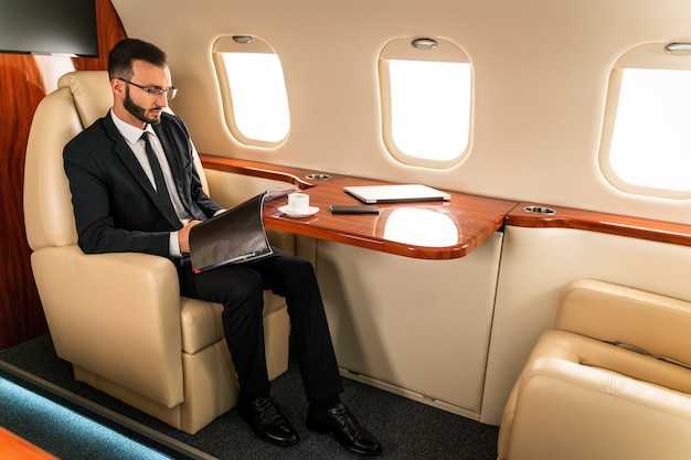 Apuesto hombre de negocios con elegante traje volando en exclusivo jet privado