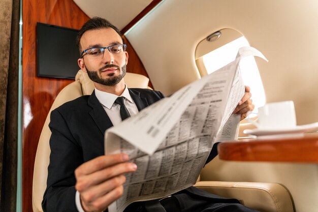 Apuesto hombre de negocios con elegante traje volando en exclusivo jet privado