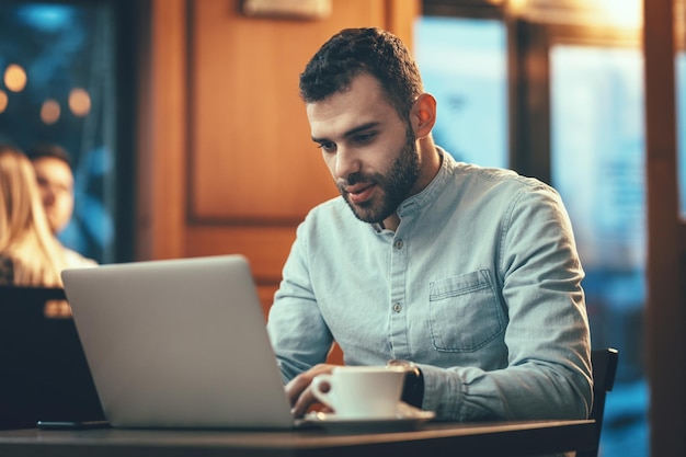 Un apuesto hombre de negocios está trabajando en una laptop y tomando café en la cafetería.