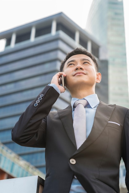 apuesto hombre de negocios hablando por teléfono móvil en el edificio de oficinas de su empresa, el modelo es un hombre asiático