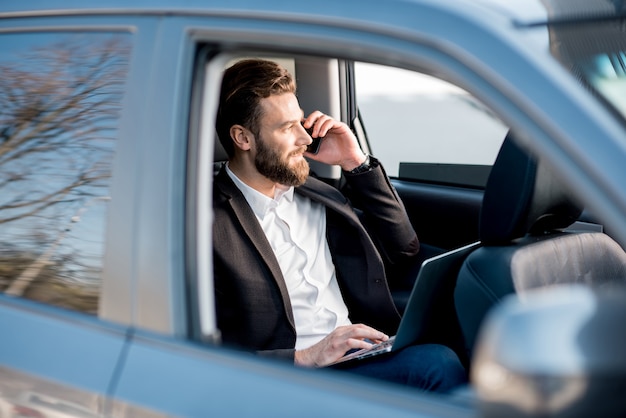 Apuesto hombre de negocios hablando con teléfono sentado en el asiento trasero del coche