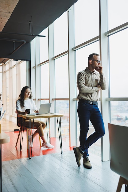 Apuesto hombre de negocios jefe asistente mujer joven dos socios trabajando juntos discutiendo proyecto espacioso gran oficina moderna interior mejores compañeros de equipo exitosos profesionales en interiores