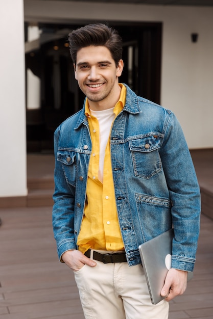 Foto apuesto hombre de negocios joven alegre feliz cerca de la cafetería al aire libre con ordenador portátil.