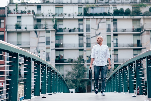 Apuesto hombre de negocios joven en una camisa blanca cruzando un puente