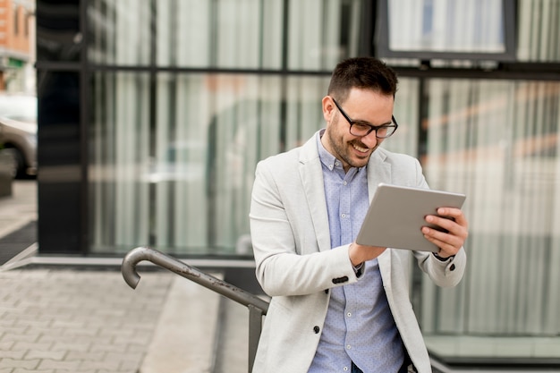 Apuesto hombre de negocios joven con tableta digital por el edificio de oficinas