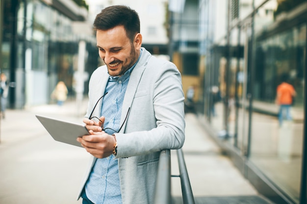 Apuesto hombre de negocios joven con tableta digital por el edificio de oficinas