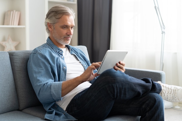 Apuesto hombre de negocios de mediana edad está usando una computadora portátil y sonriendo mientras trabaja en casa.