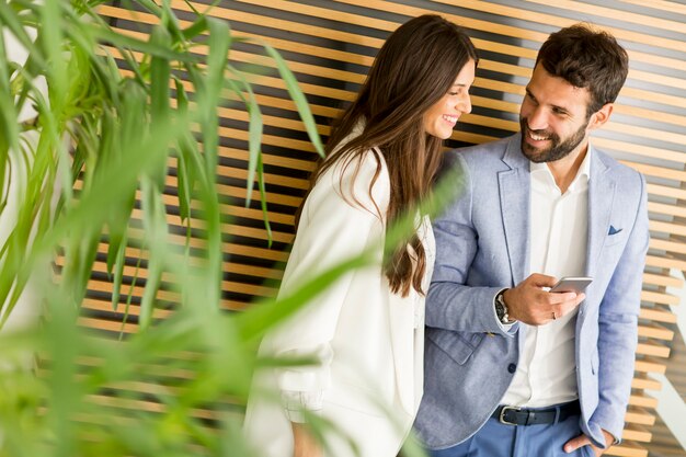 Apuesto hombre de negocios y mujer mirando smartphone juntos en la oficina moderna