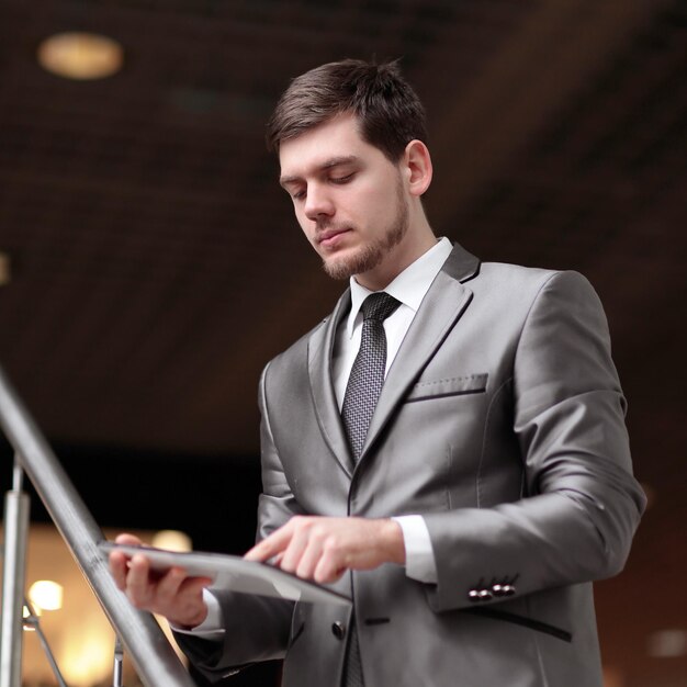 Apuesto hombre de negocios de pie sobre pasos usando tableta en edificio de oficinas