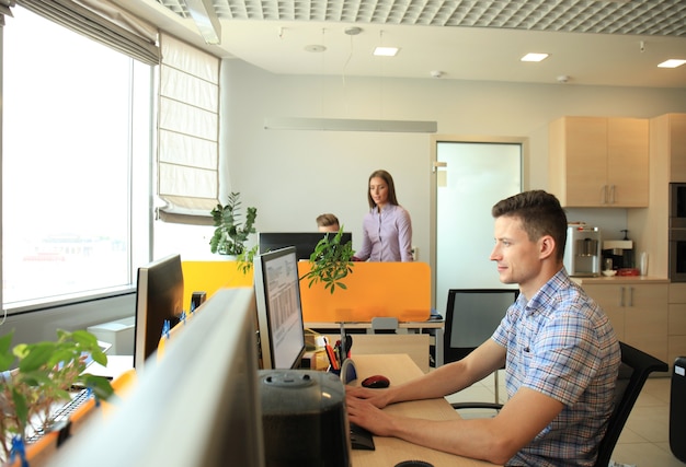 Apuesto hombre de negocios en ropa casual en el fondo de sus socios en la oficina creativa