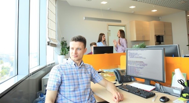 Apuesto hombre de negocios en ropa casual en el fondo de sus socios en la oficina creativa