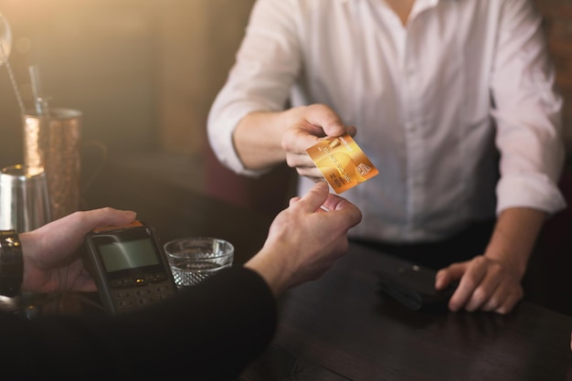 Apuesto hombre de negocios en ropa formal dando tarjeta de crédito al barman mientras está sentado en el bar, copie el espacio, primer plano