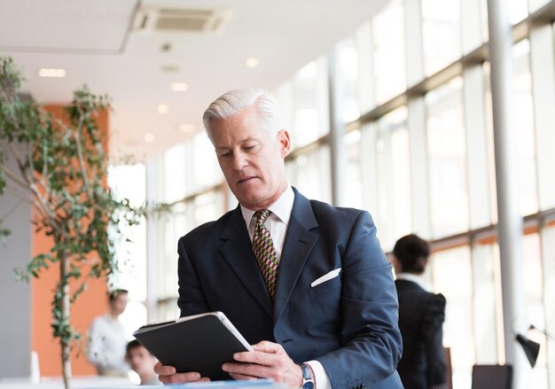 apuesto hombre de negocios senior con cabello gris que trabaja en una tableta en el moderno y luminoso interior de la oficina