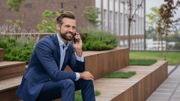 Apuesto hombre de negocios sonriente vistiendo elegante traje hablando por teléfono móvil en la calle