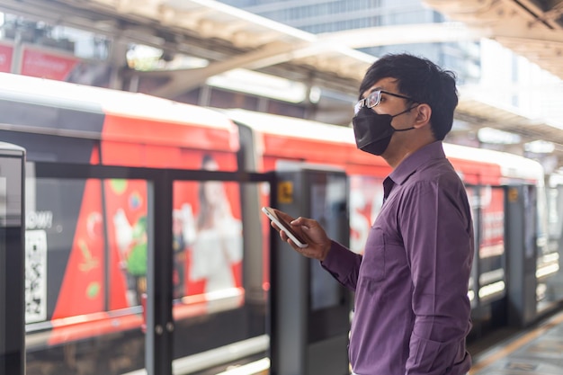 Apuesto hombre de negocios sosteniendo el teléfono en la estación de tren del cielo en Bangkok