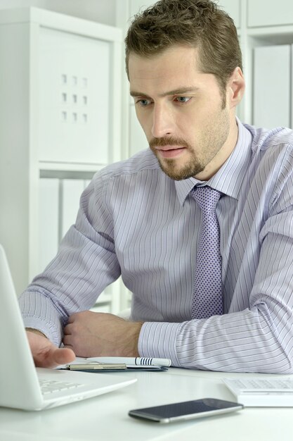 Foto apuesto hombre de negocios trabajando con ordenador portátil en la oficina