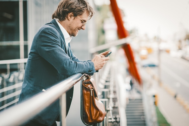 Apuesto hombre de negocios trabajando en smarphone fuera del centro de negocios