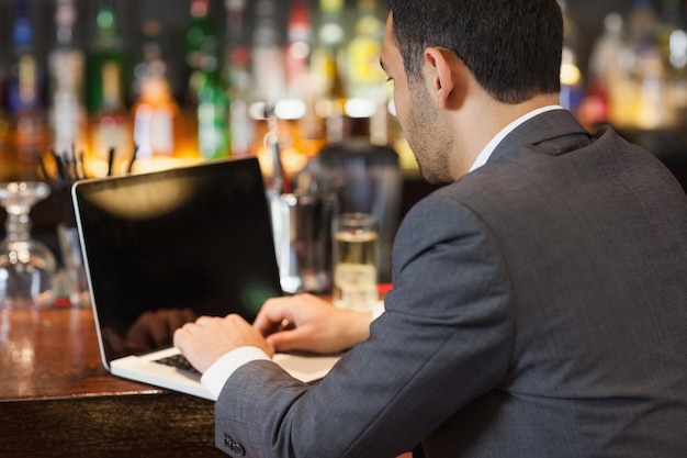 Apuesto hombre de negocios trabajando en su computadora portátil mientras toma una copa
