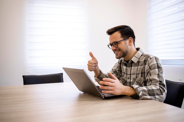 Apuesto hombre de negocios trabajando en su computadora portátil y teniendo una reunión en línea en su oficina