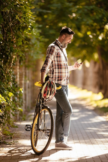 Apuesto hombre de negocios va a trabajar en bicicleta. Está parado al lado de la bicicleta y usando un teléfono inteligente.